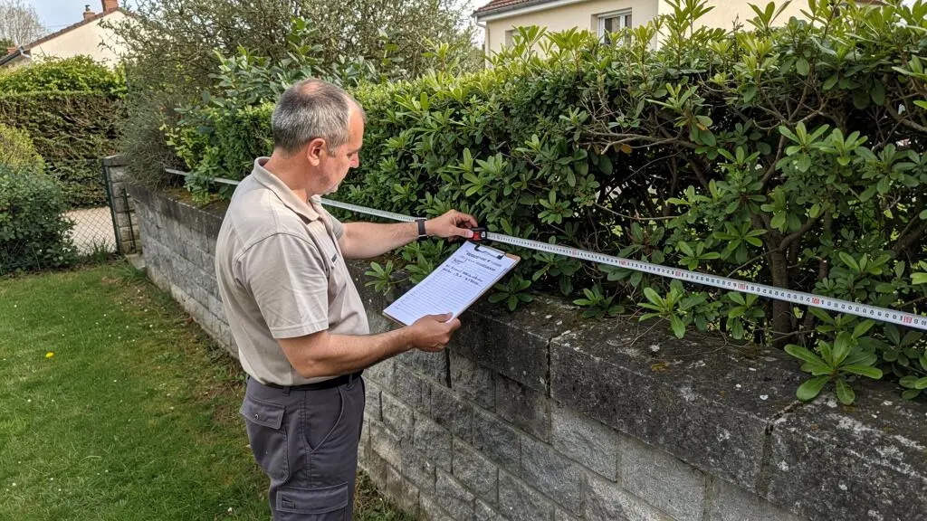 Commissaire de justice mesurant une haie qui empiète sur la limite de propriété entre deux voisins dans un jardin résidentiel français